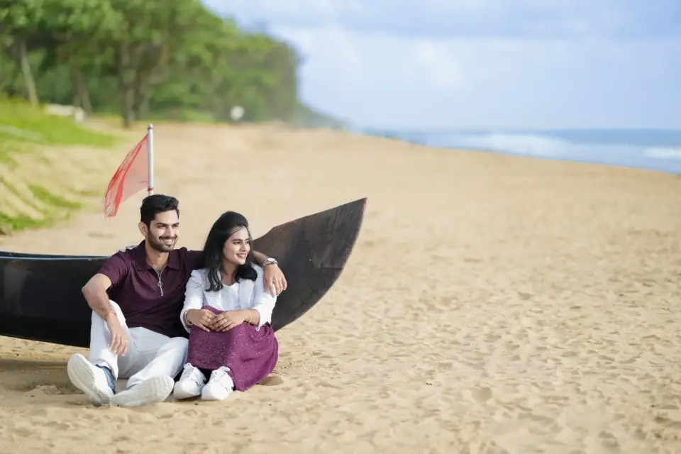 Couple sitting beside a fishing boat on a palm-lined beach