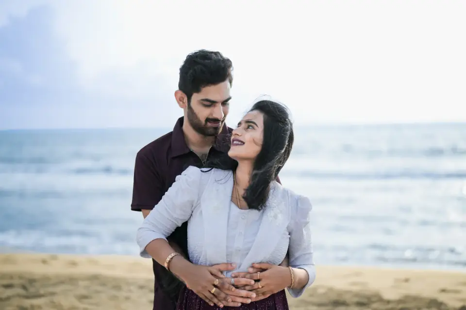 Expecting couple on the beach, his hands resting on her bump