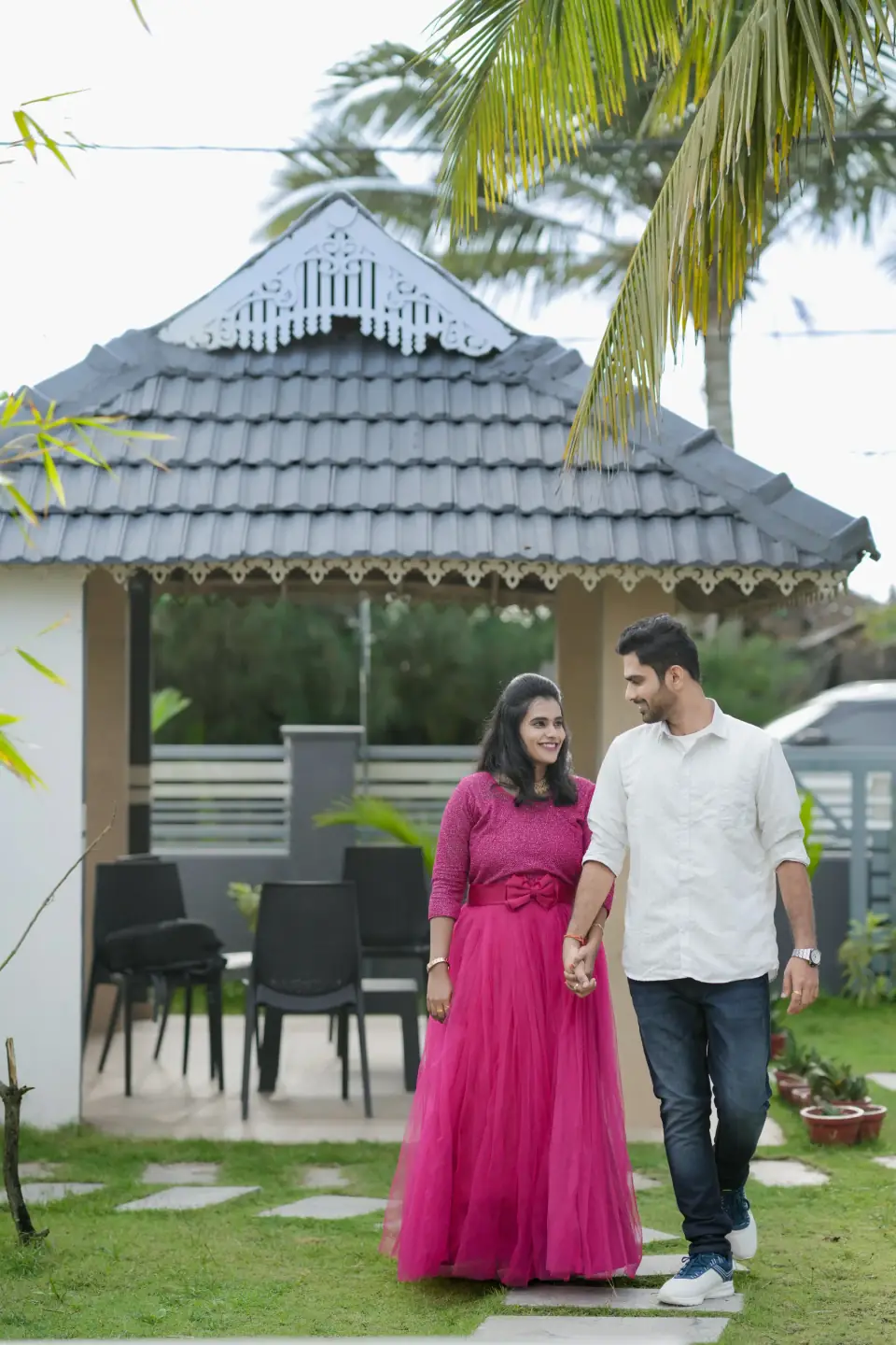 Expecting couple walking in front of a garden cottage