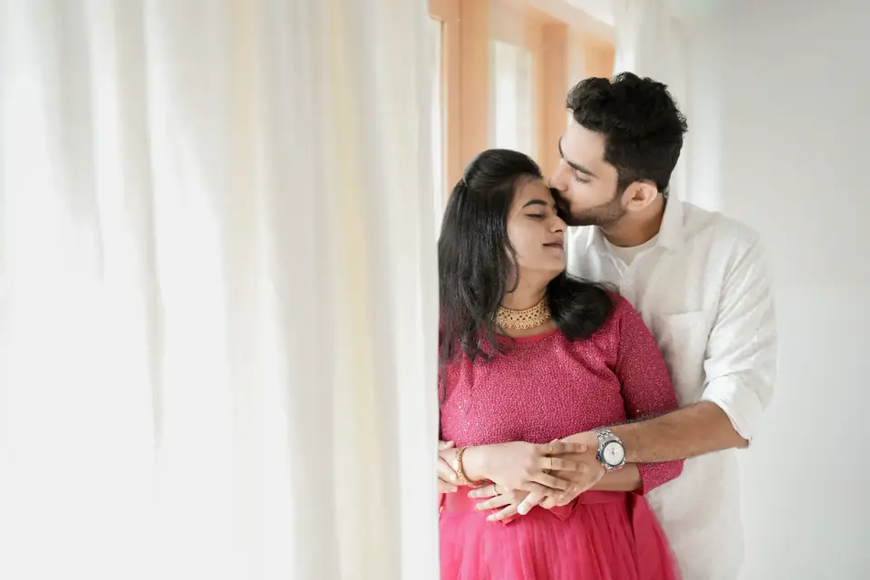 Soft window-light maternity portrait of a couple in pink and white