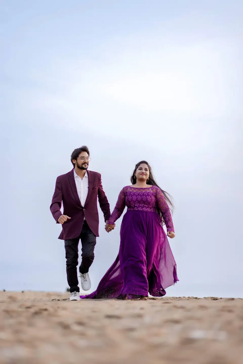 Couple striding together across the sand under a pale sky