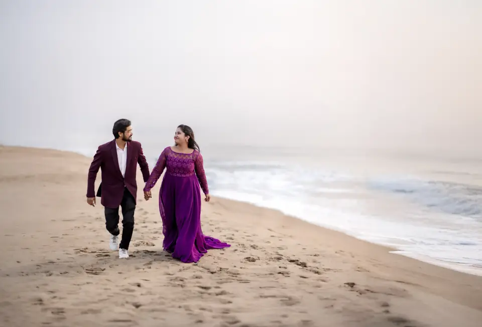 Couple walking barefoot along the beach at dawn