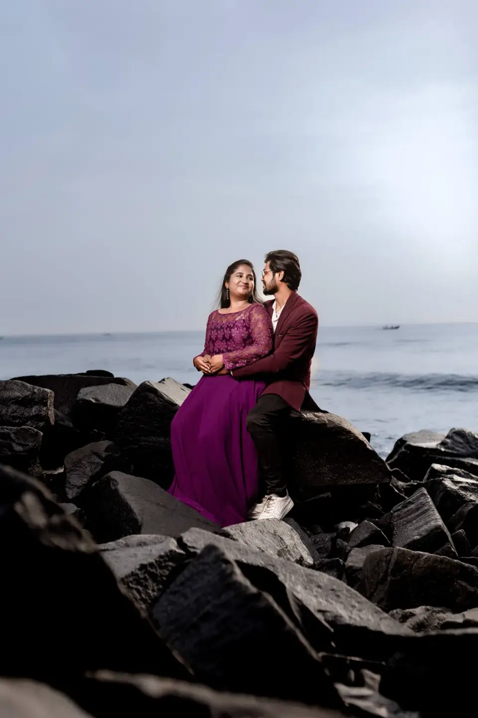 Couple standing on black rocks against a soft grey sea