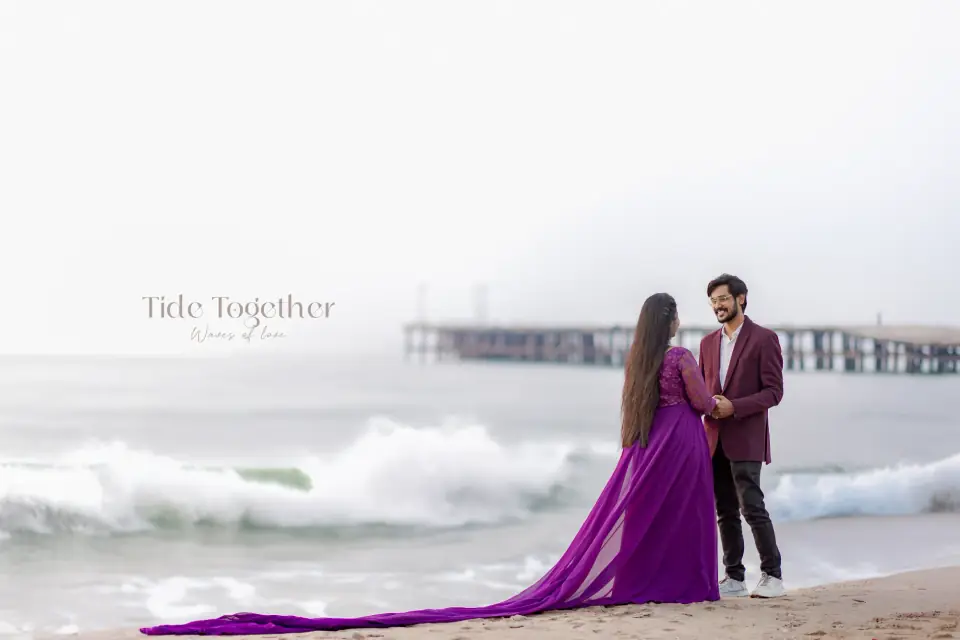 Couple by crashing waves near a pier, the gown spread across the sand